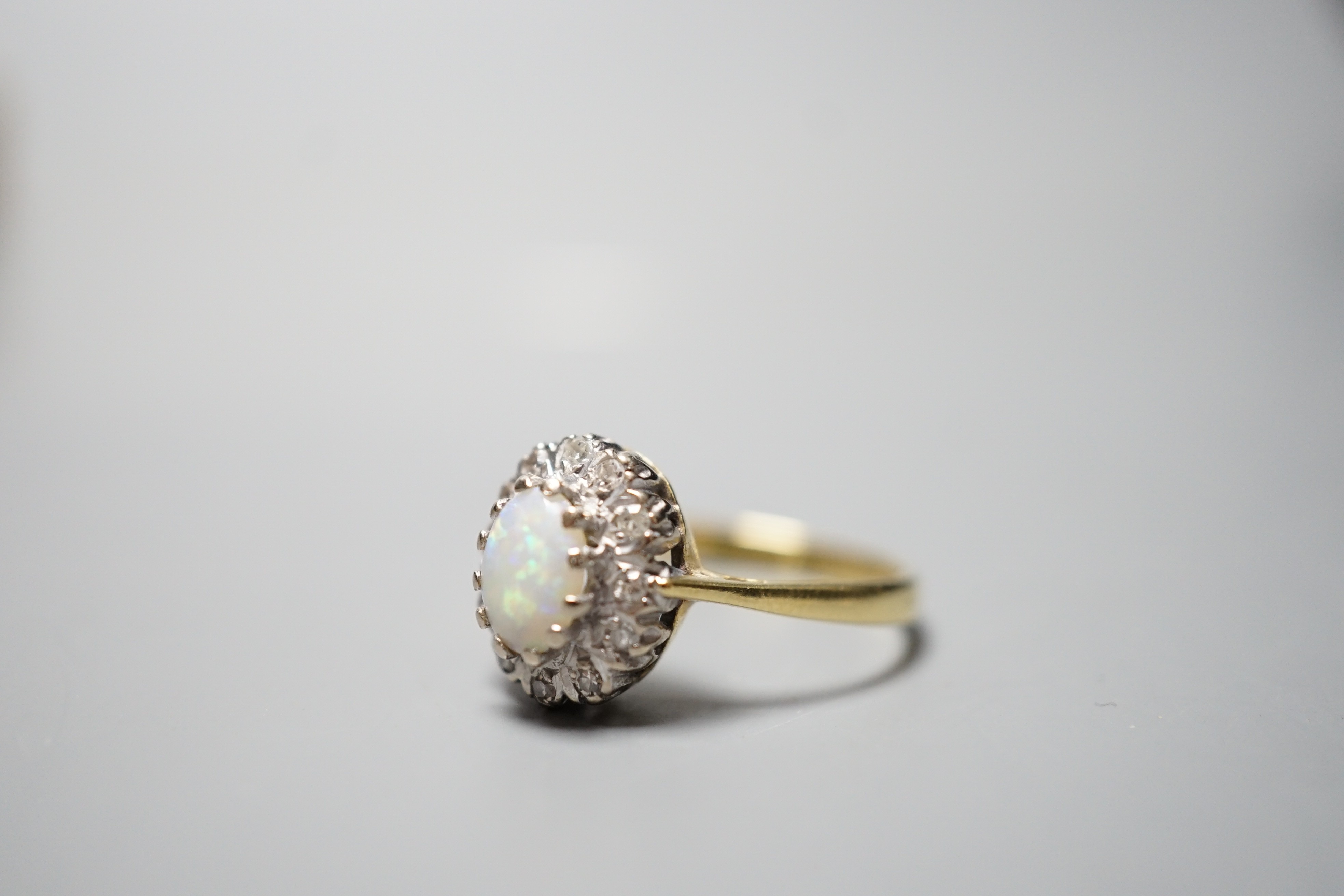 A modern 18ct gold, white opal and diamond chip set oval cluster ring, size N, gross weight 3.6 grams.